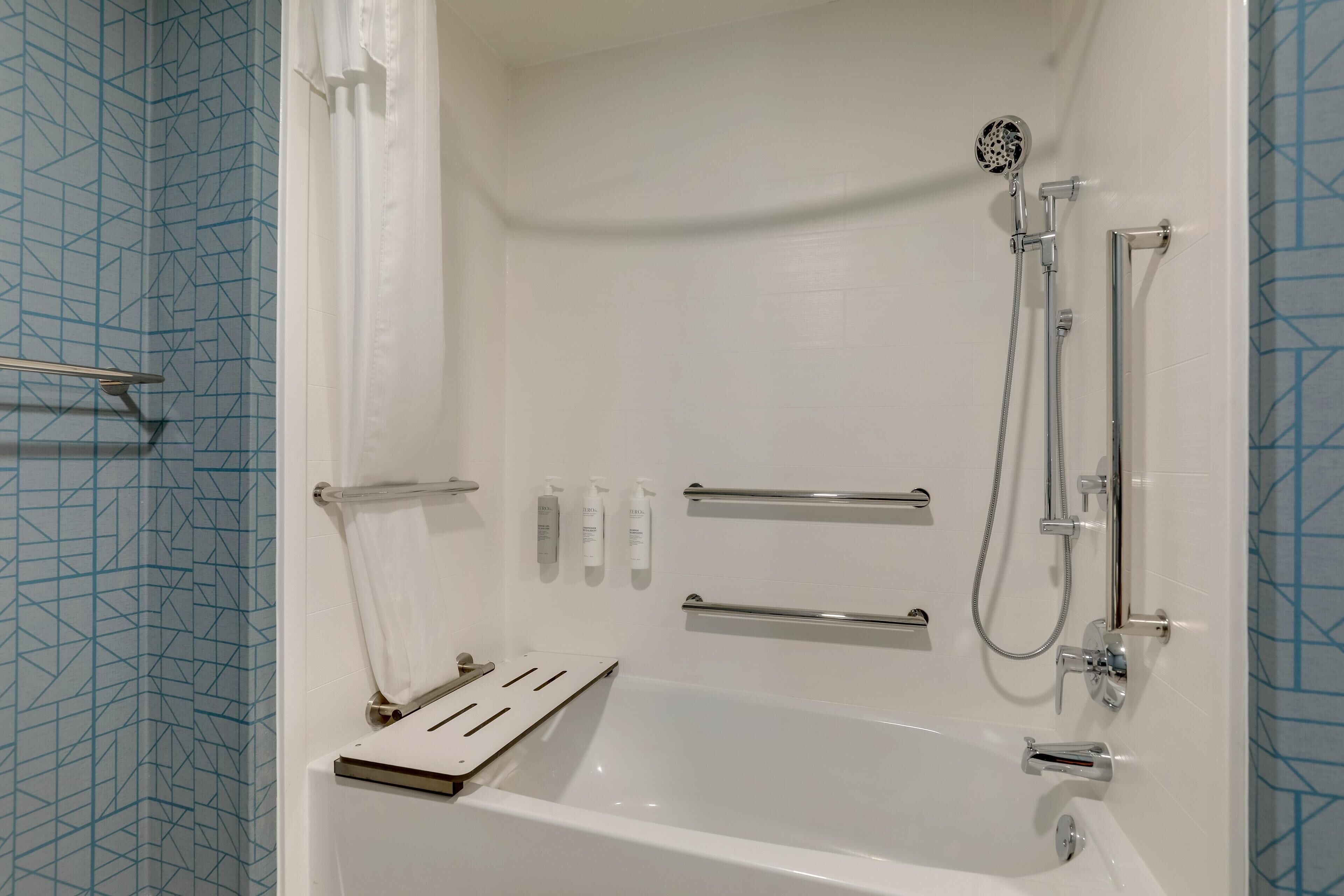 Een moderne badkamer met een bad, douche en handgrepen.