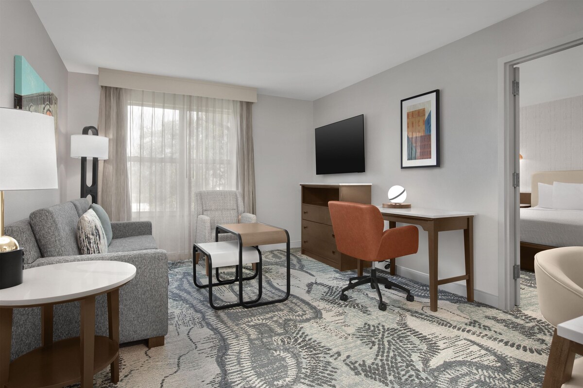 A hotel room with a sofa, a desk, a chair, a TV, and a bed.