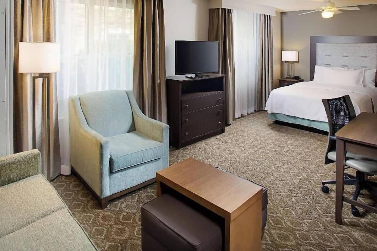 A hotel room with a bed, a television on a dresser, a desk with a chair, and a sofa.