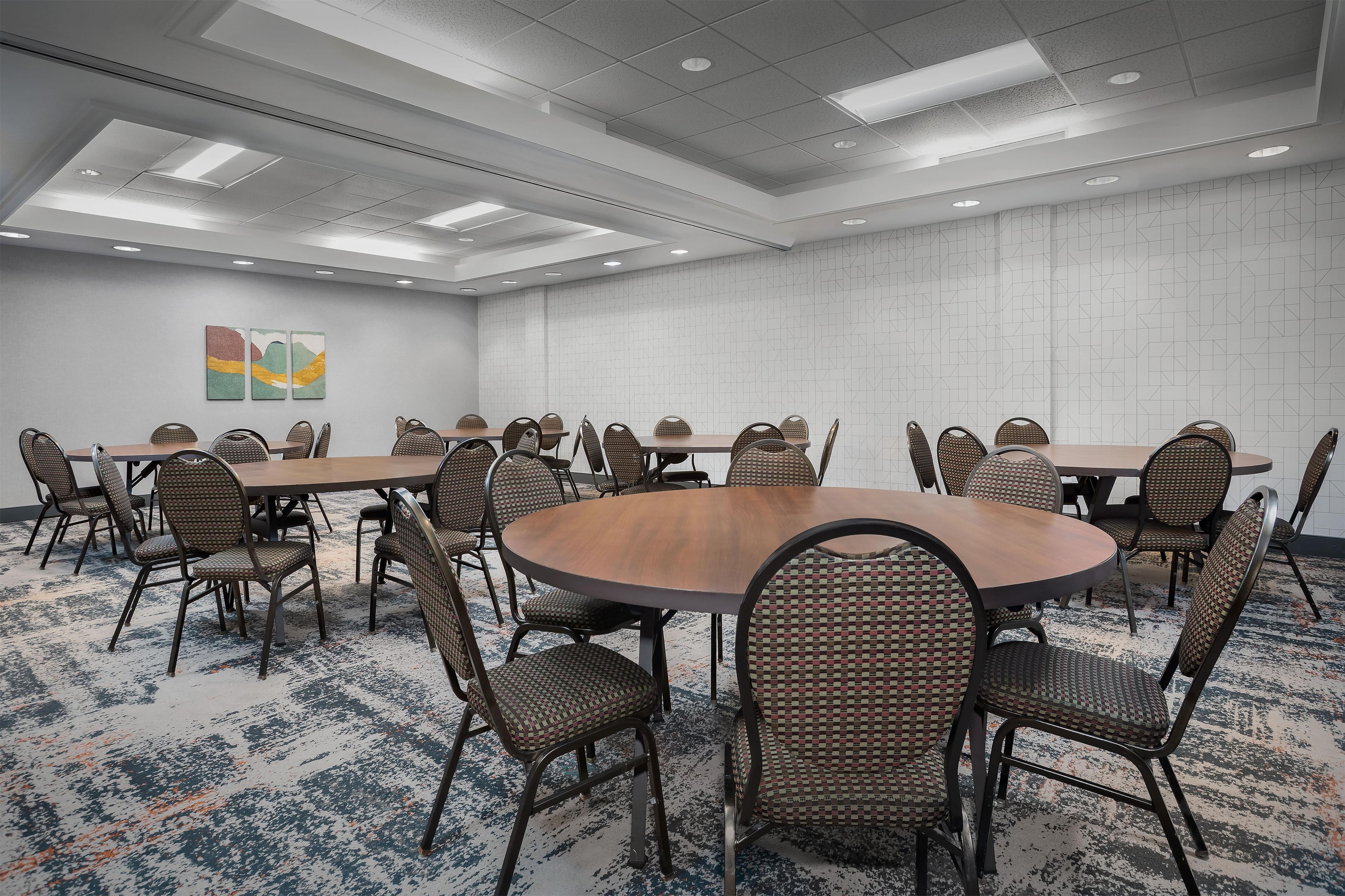 A conference room with round tables and wicker chairs, a patterned carpet, and a geometric wall design.