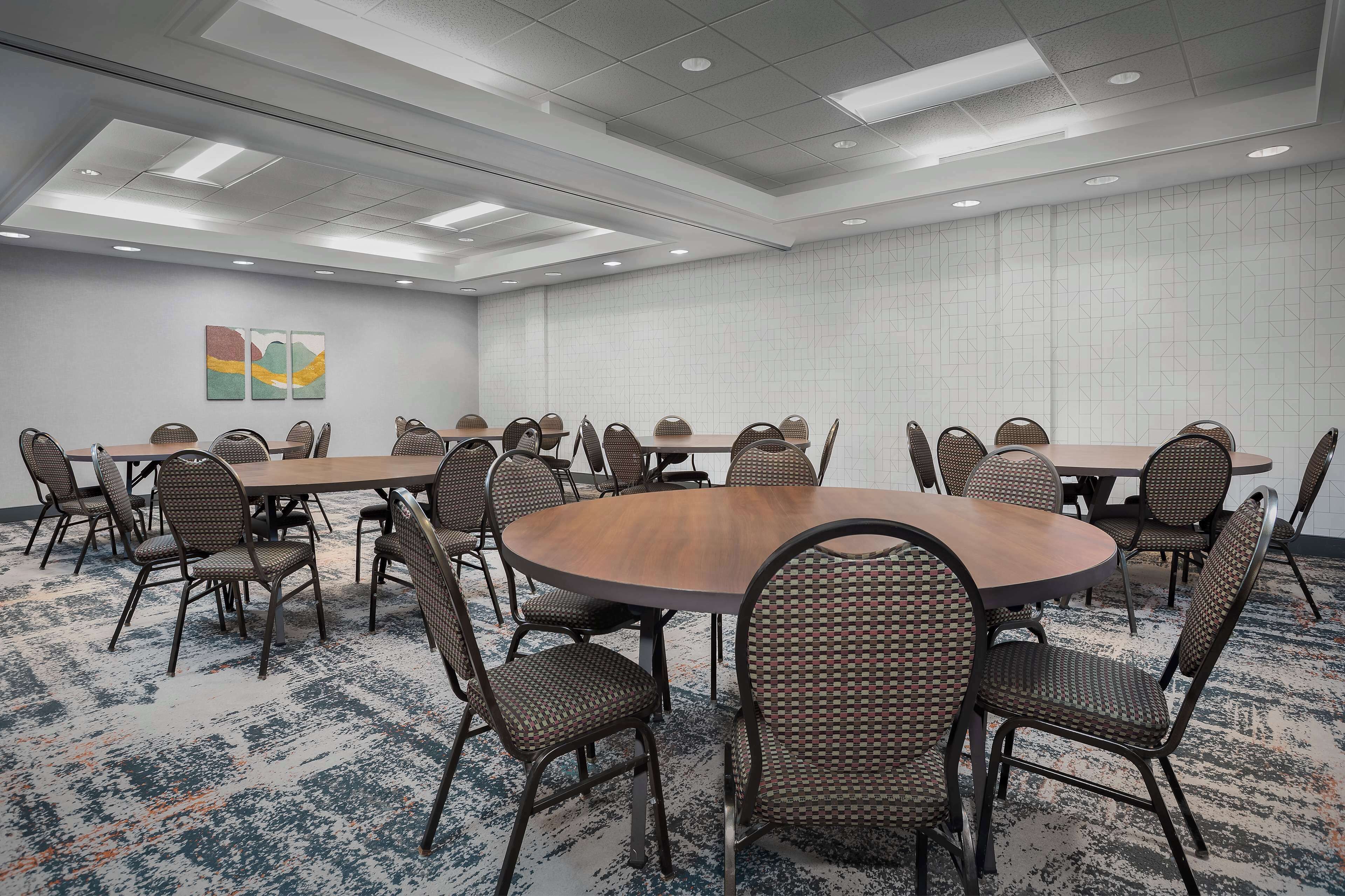A conference room with multiple tables and chairs, a patterned carpet, and a ceiling with recessed lighting.