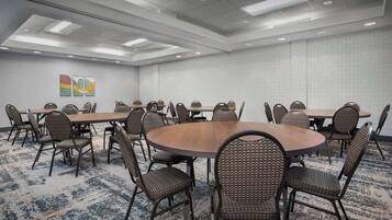 A conference room with multiple tables and chairs, a patterned carpet, and a ceiling with recessed lighting.