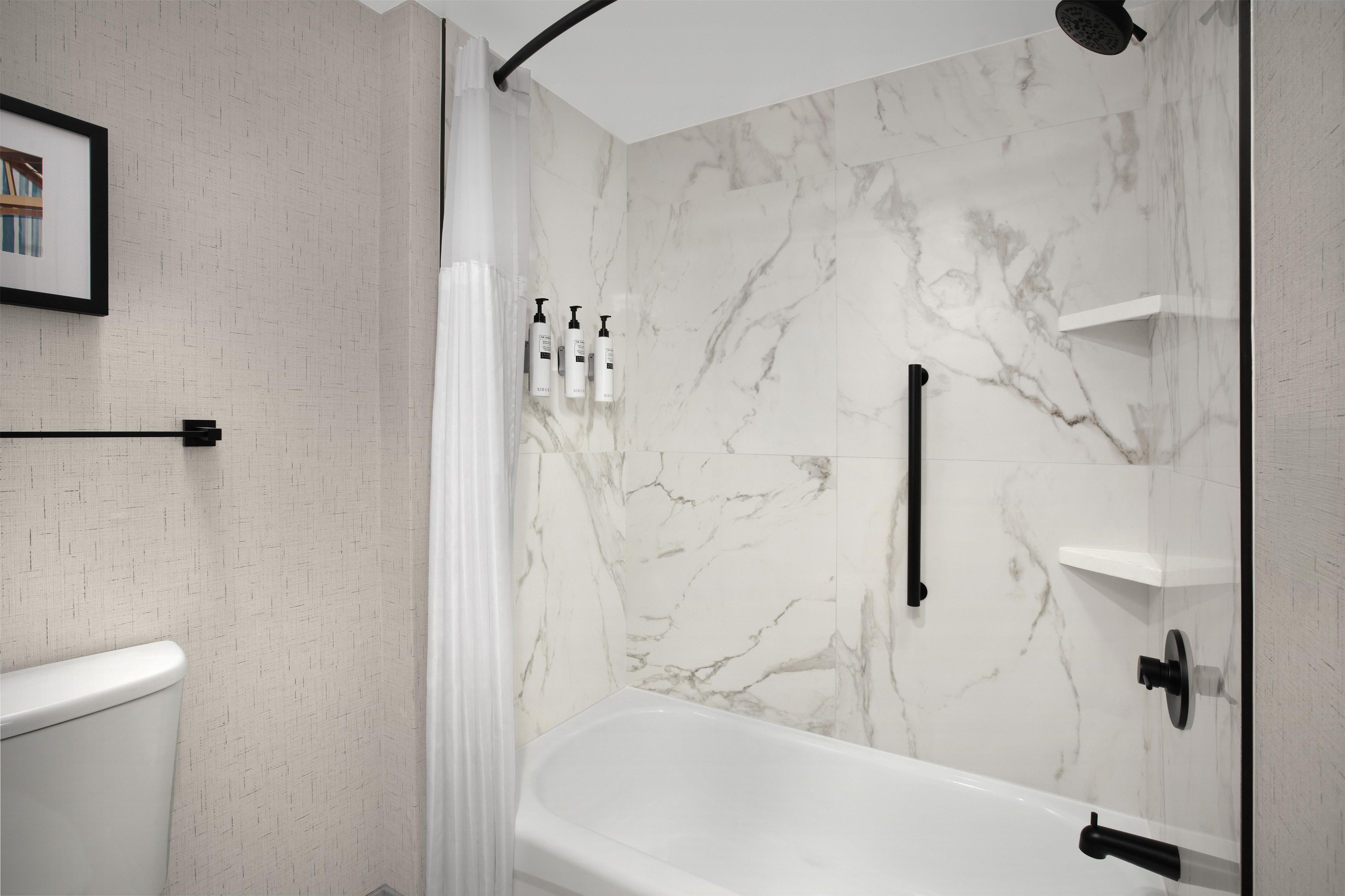 A modern bathroom with a marble shower wall, a white bathtub, and a toilet.