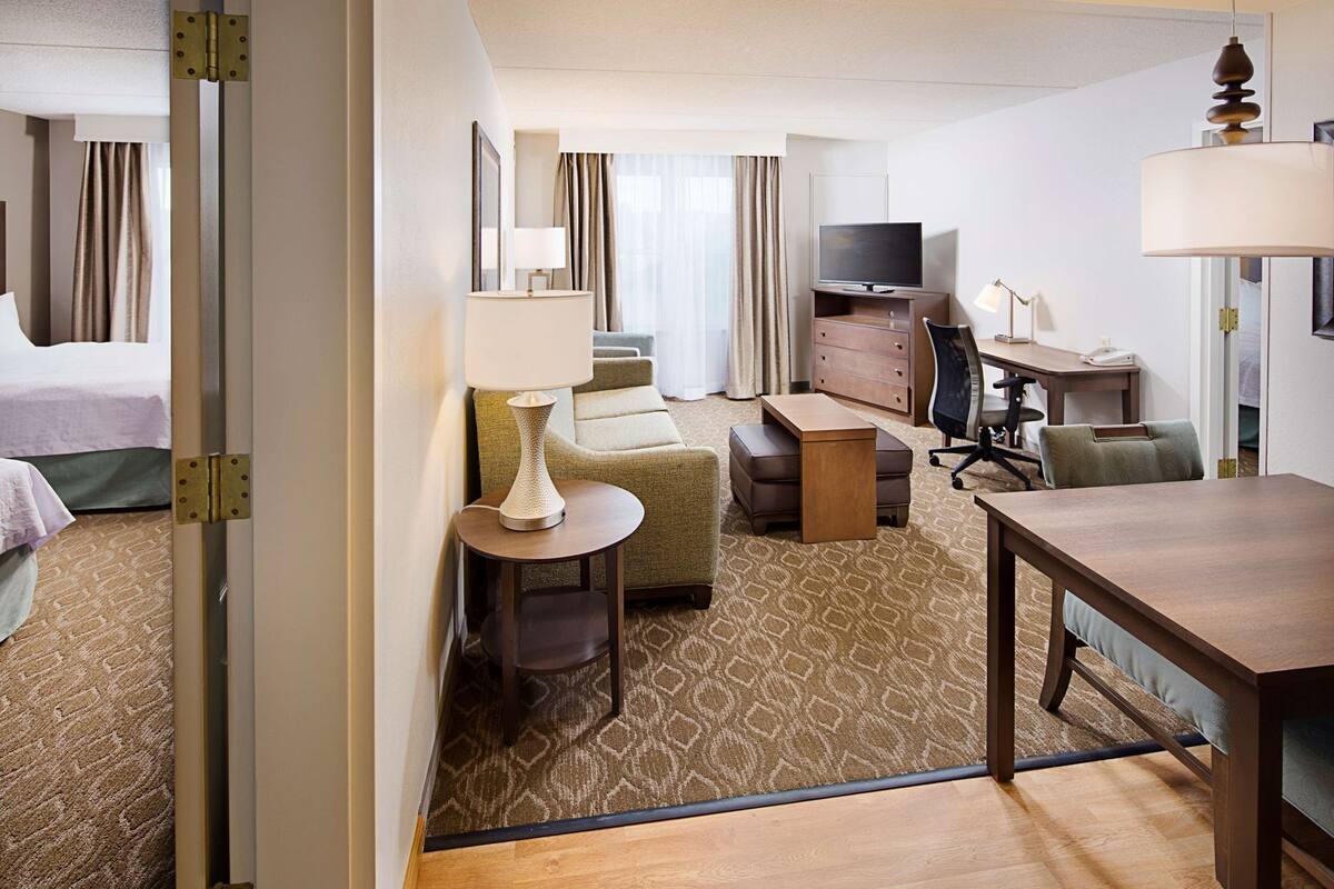A hotel room with a bed, a desk, a chair, a television, and a lamp.