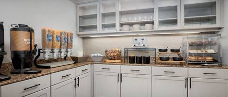 A modern kitchen with white cabinets, a coffee station, and a glass display case.