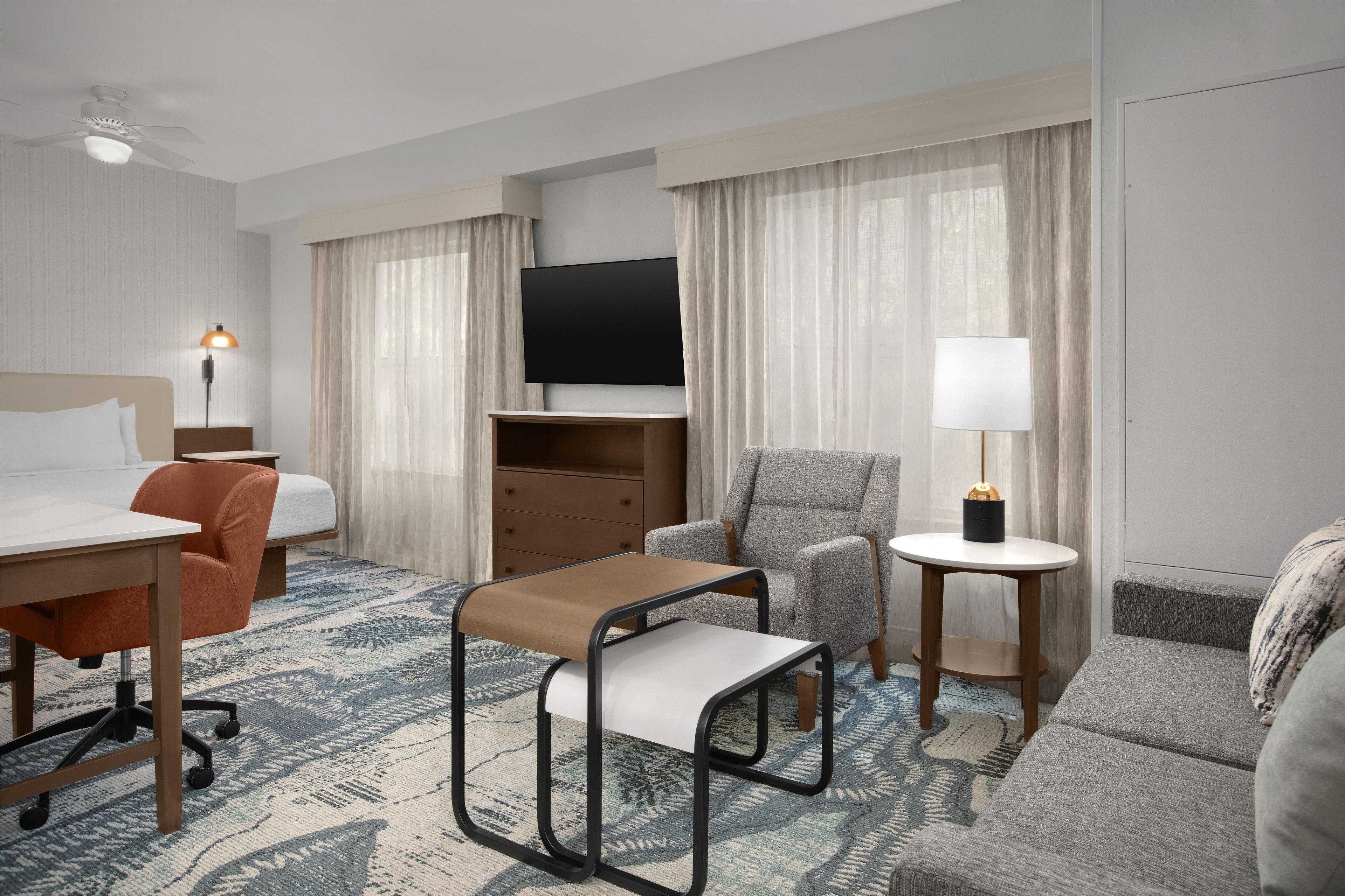 A hotel room with a bed, a desk, a chair, a sofa, a TV, and a lamp.