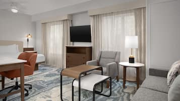 A hotel room with a bed, a desk, a chair, a sofa, a TV, and a lamp.
