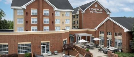 A hotel with a brick facade, outdoor seating area, and a sign reading 'Homewood Suites by Hilton'.