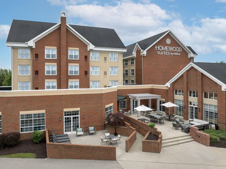 A hotel with a brick facade, outdoor seating area, and a sign reading 'Homewood Suites by Hilton'.