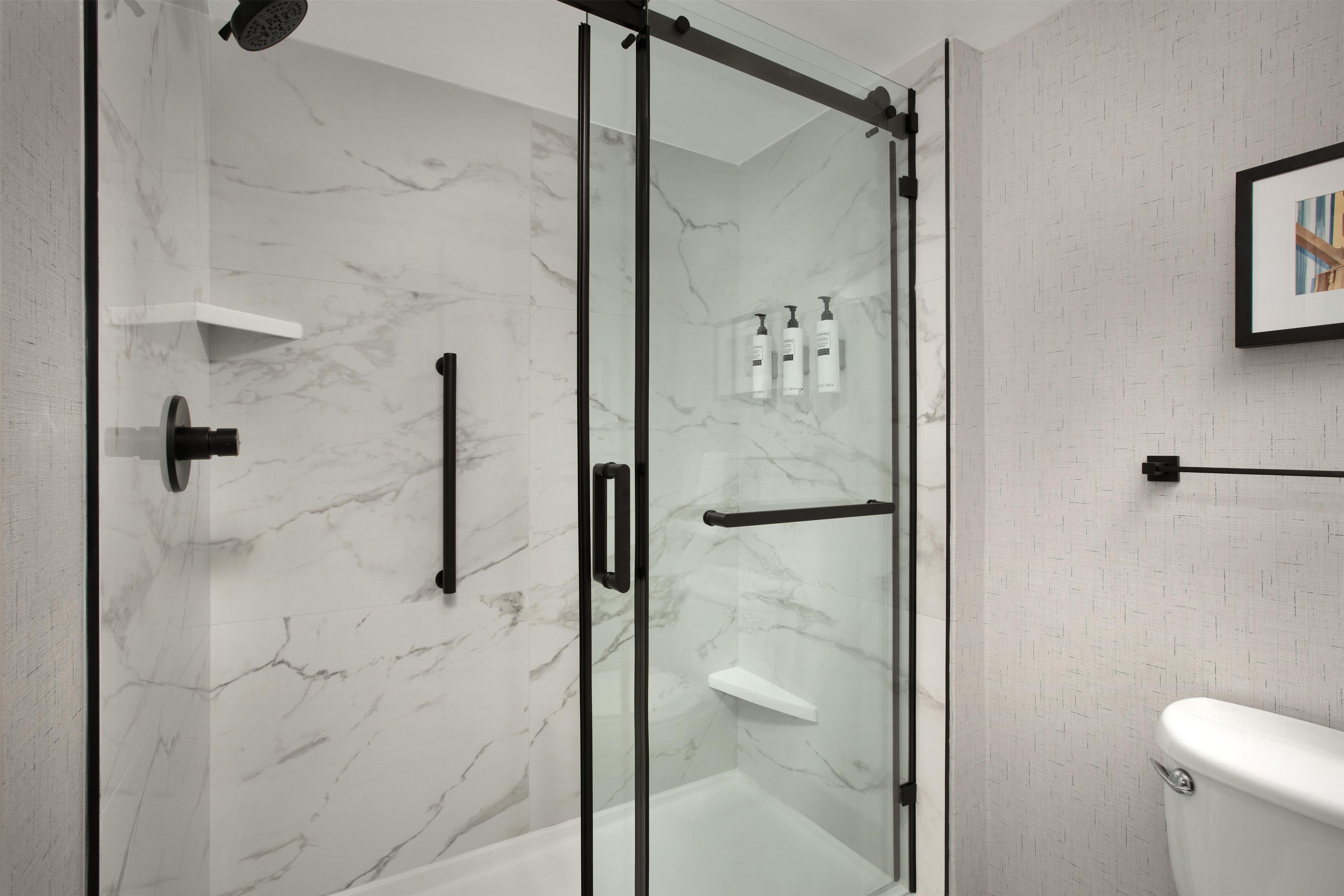 Un baño moderno con cabina de ducha de vidrio, inodoro y un cuadro en la pared.