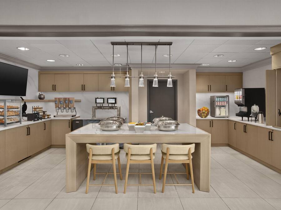 Una cocina moderna con una isla central, taburetes de bar, un televisor de pantalla plana y una cafetera.