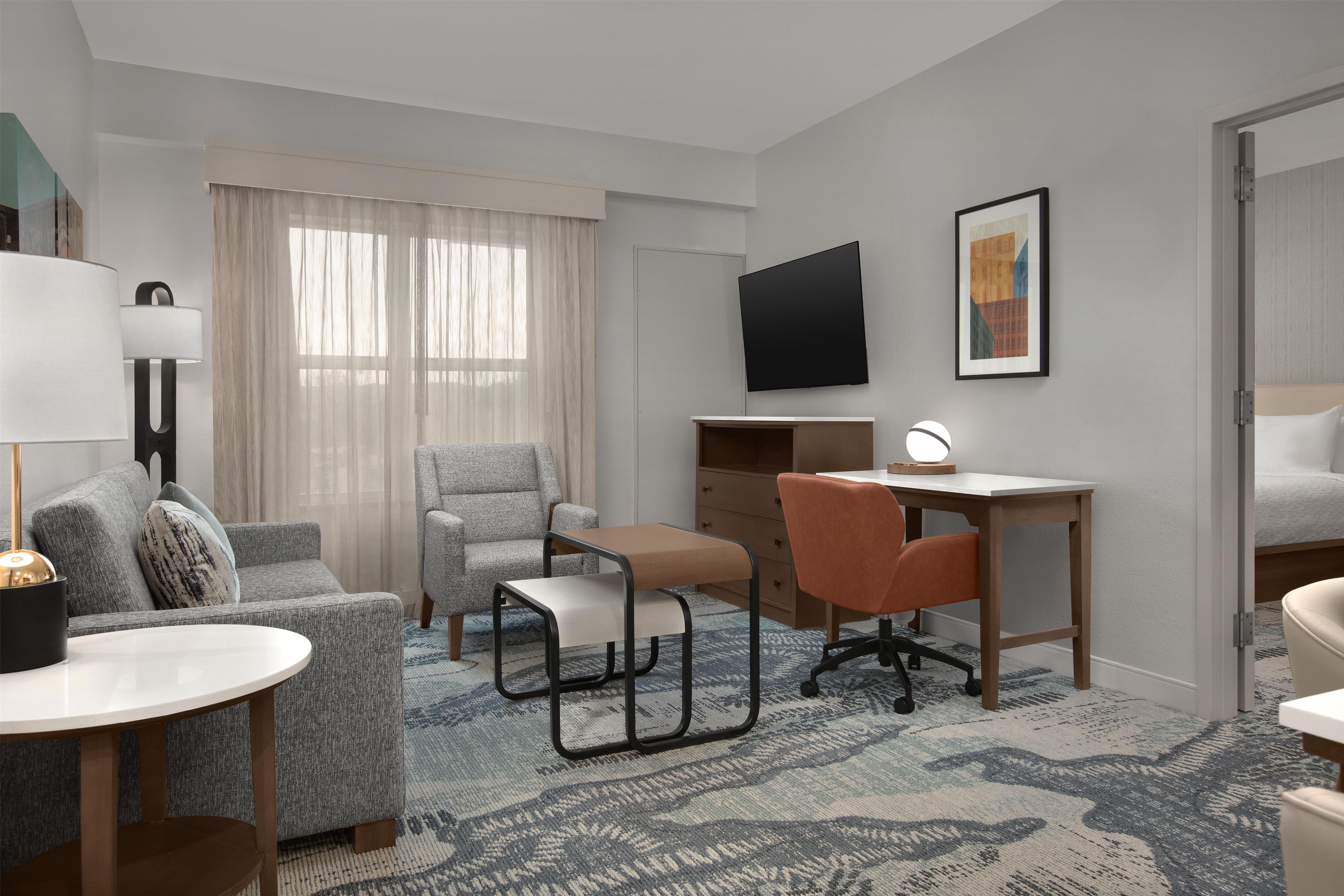 A hotel room with a bed, a desk, a chair, a sofa, a TV, and a lamp.