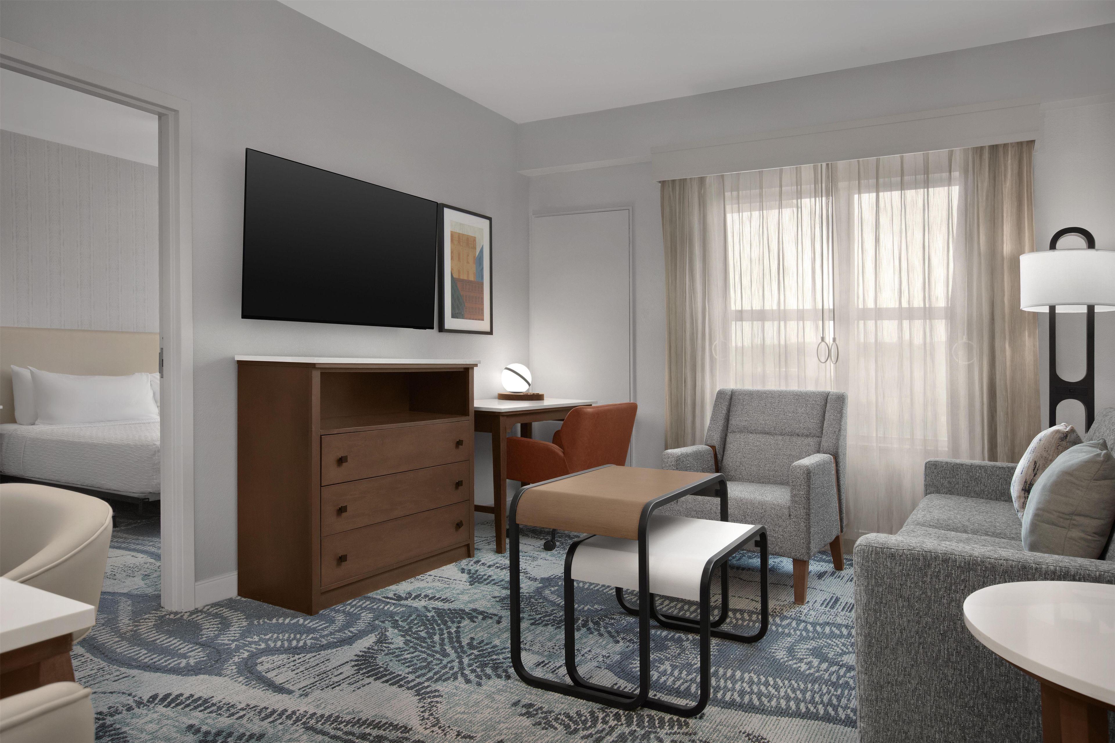 Ein Hotelzimmer mit Bett, Schreibtisch, Sessel, Sofa und Fernseher.