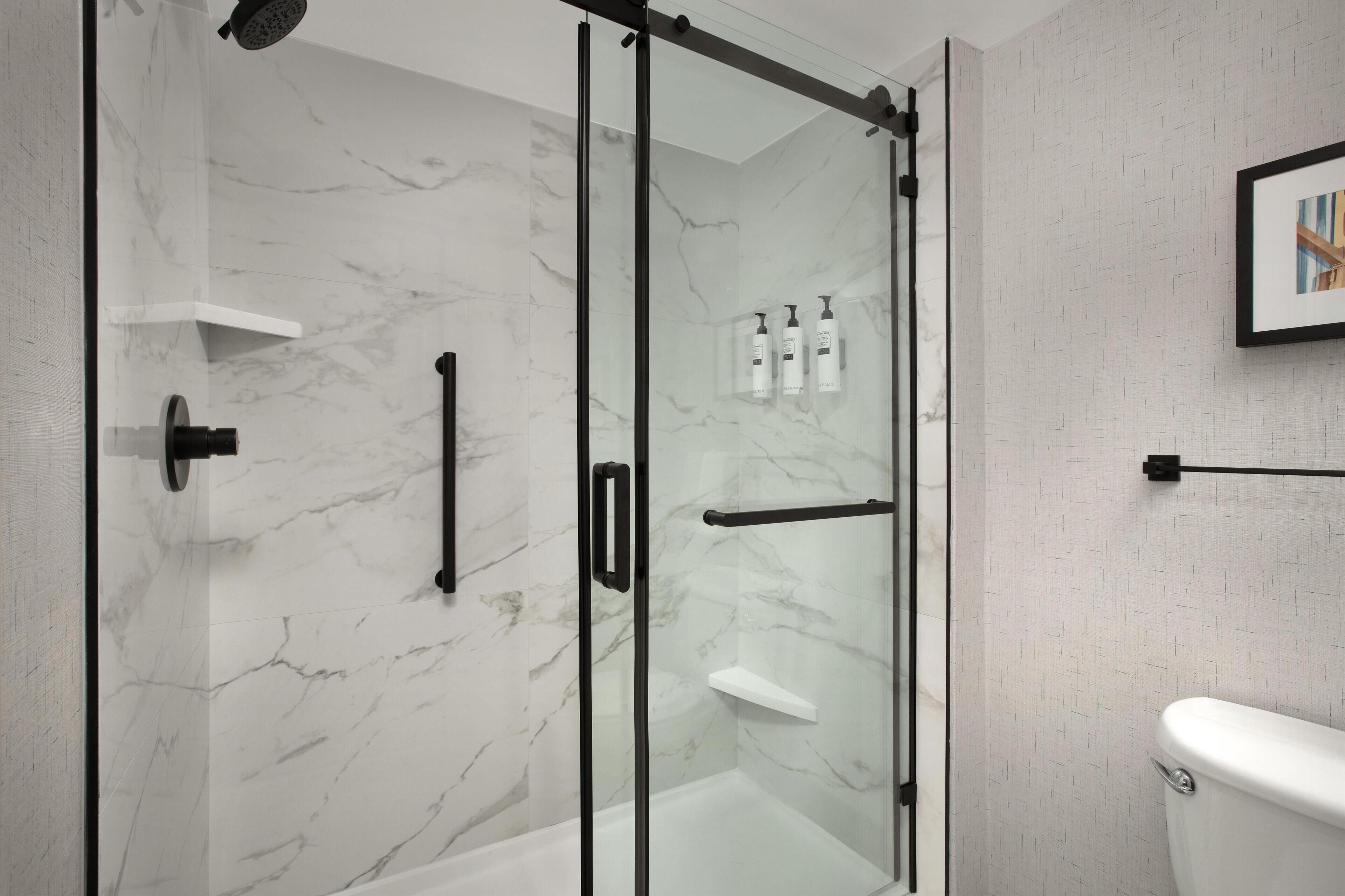 Une salle de bain moderne avec une douche à parois de verre, des toilettes et un tableau encadré au mur.