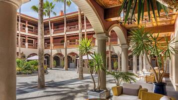 A spacious courtyard with palm trees, outdoor seating, and a multi-level building with balconies.