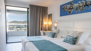 Habitación de hotel con dos camas, un escritorio, una silla, una lámpara y vistas a un puerto deportivo y al horizonte urbano.