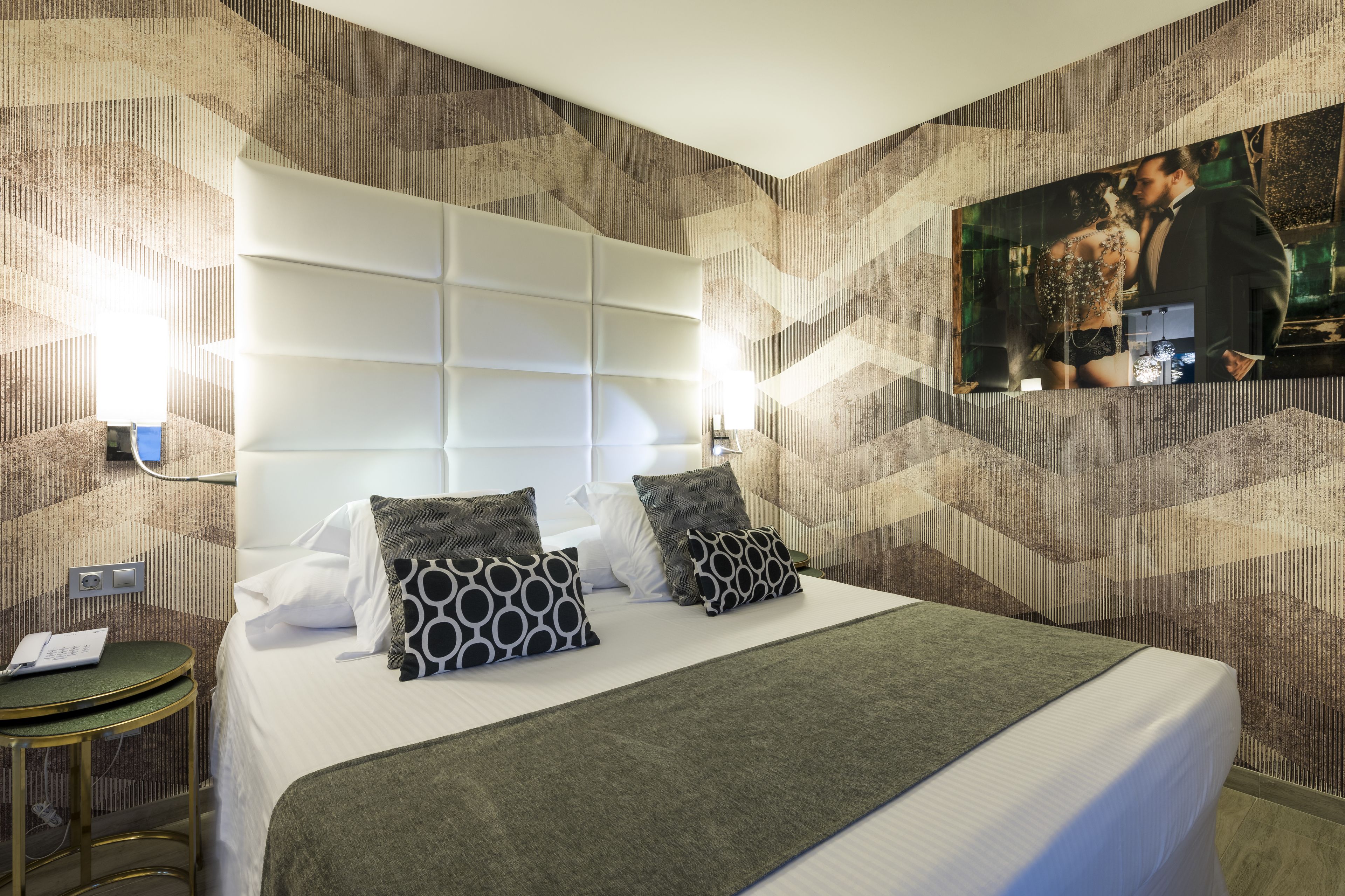Habitación de hotel con una cama grande, cabecera, una mesita pequeña y televisor montado en la pared.