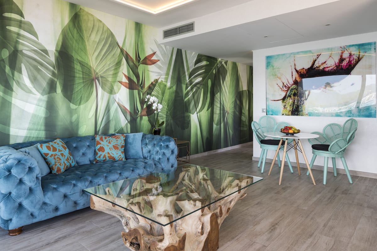 A modern living room with a blue sofa, glass coffee table, and a dining area with teal chairs and a small table.