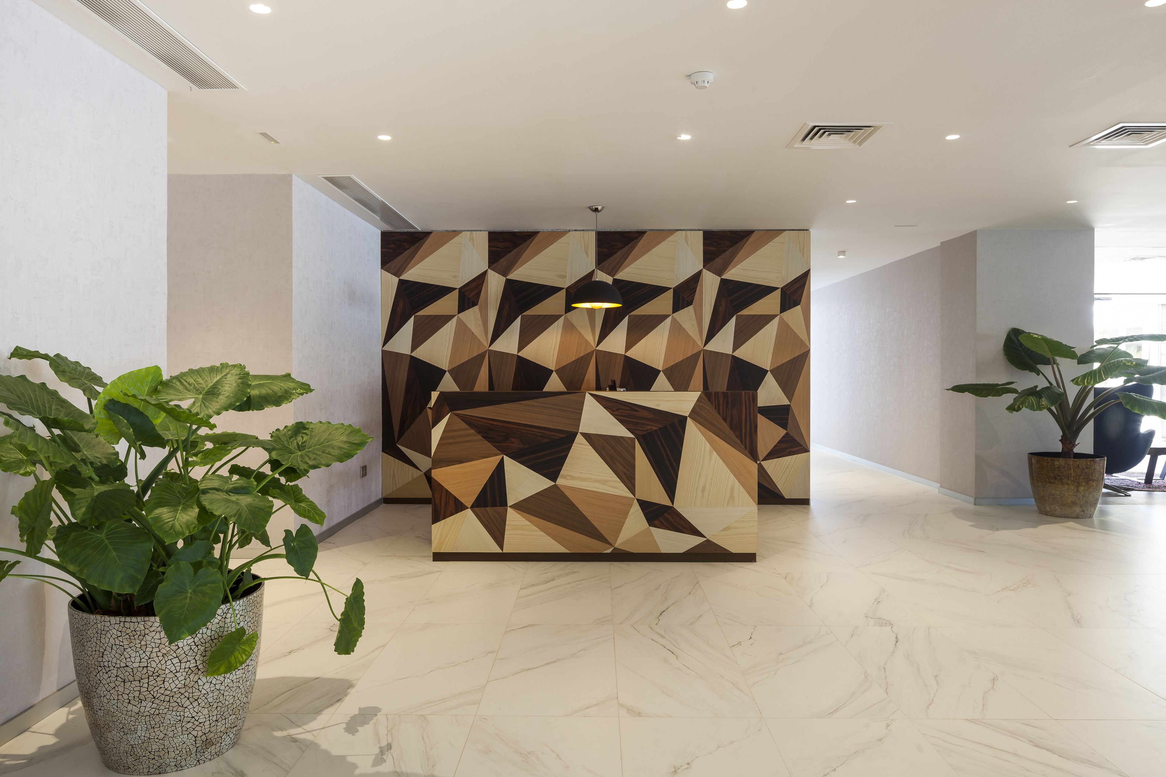A modern lobby with a geometric-patterned wall, a marble floor, and potted plants.