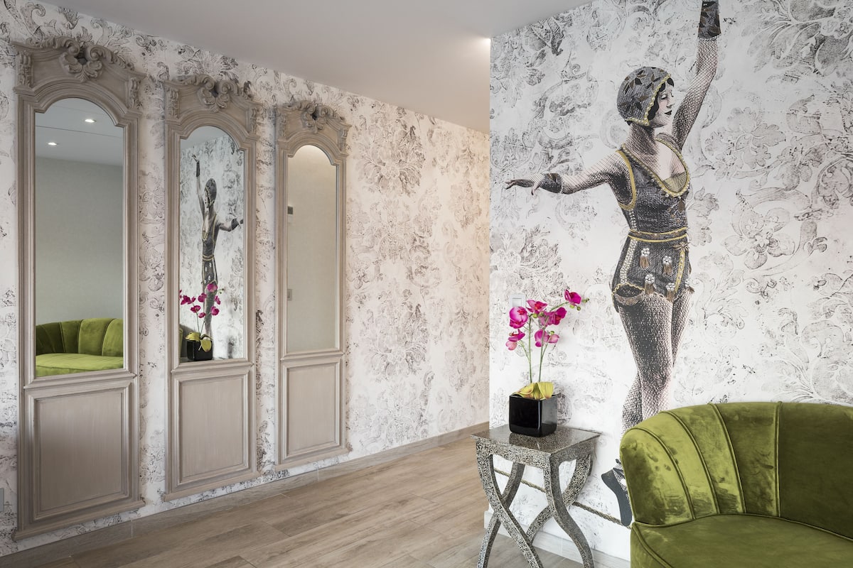 A room with a green sofa, a small table with a vase of flowers, and a large wall mural.