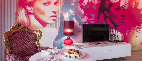 Une pièce moderne avec une table à manger ronde, un téléviseur et une grande fresque murale.