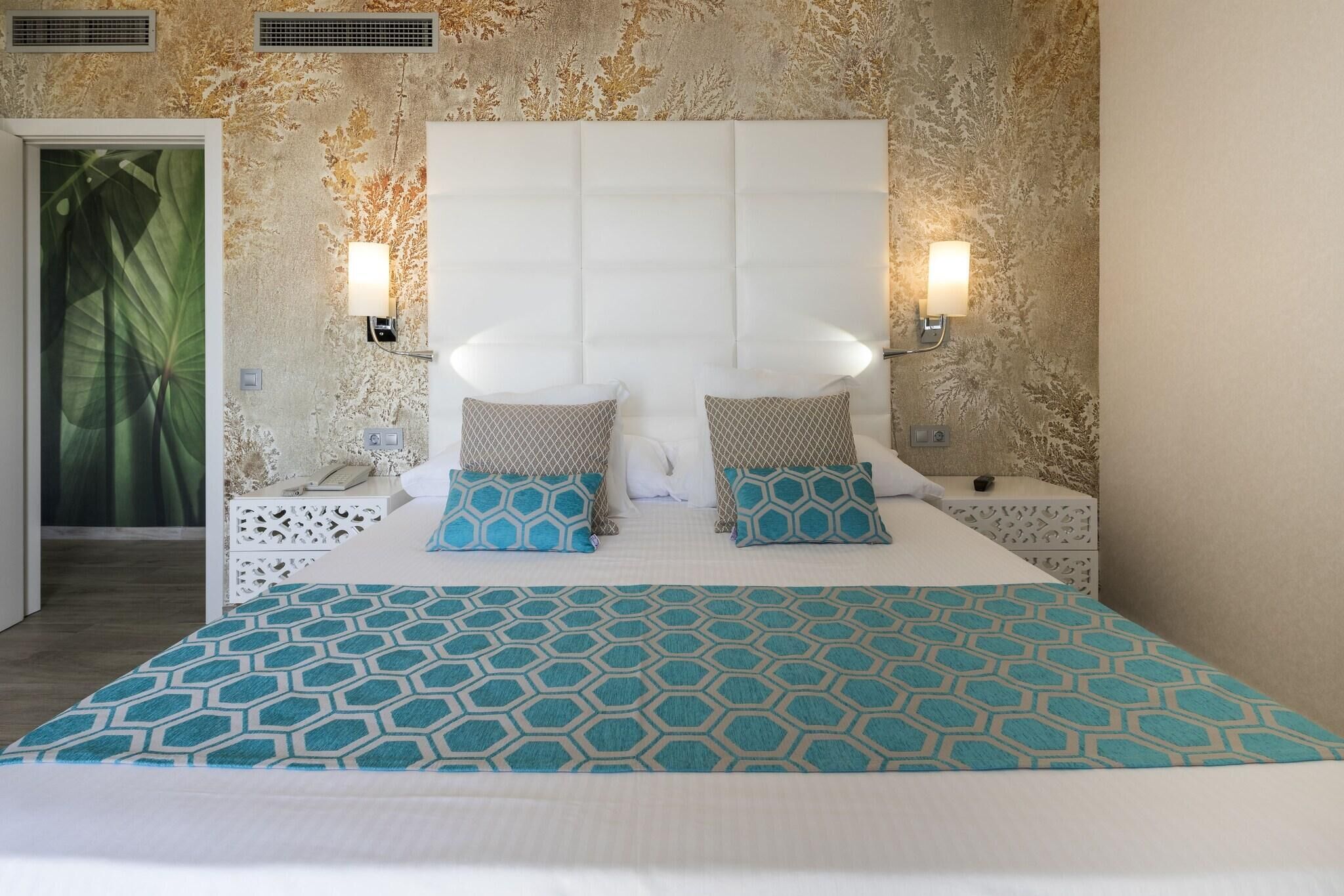 A bed with a geometric patterned bedspread, a tufted headboard, and two bedside lamps.