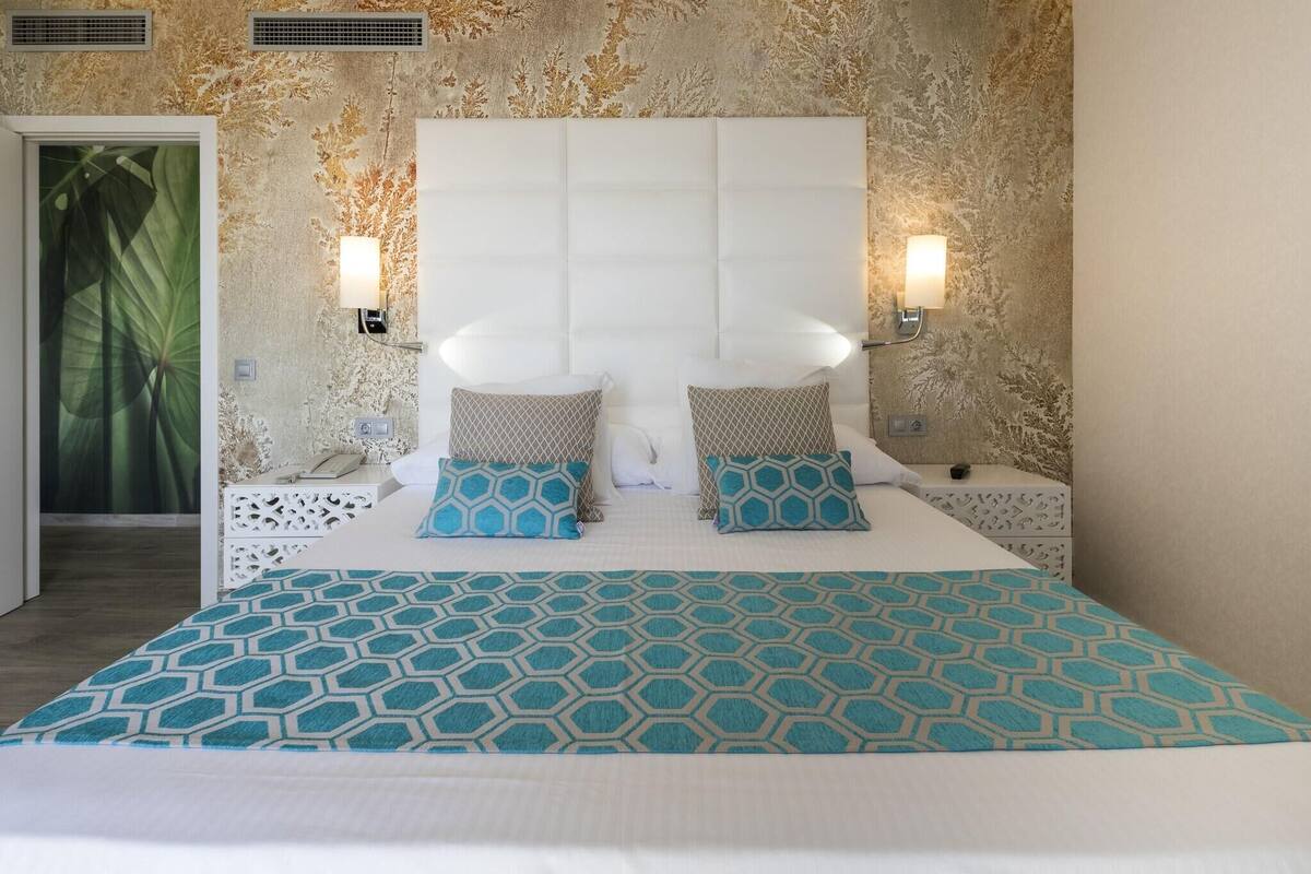 A bed with a geometric patterned bedspread, a tufted headboard, and two bedside lamps.