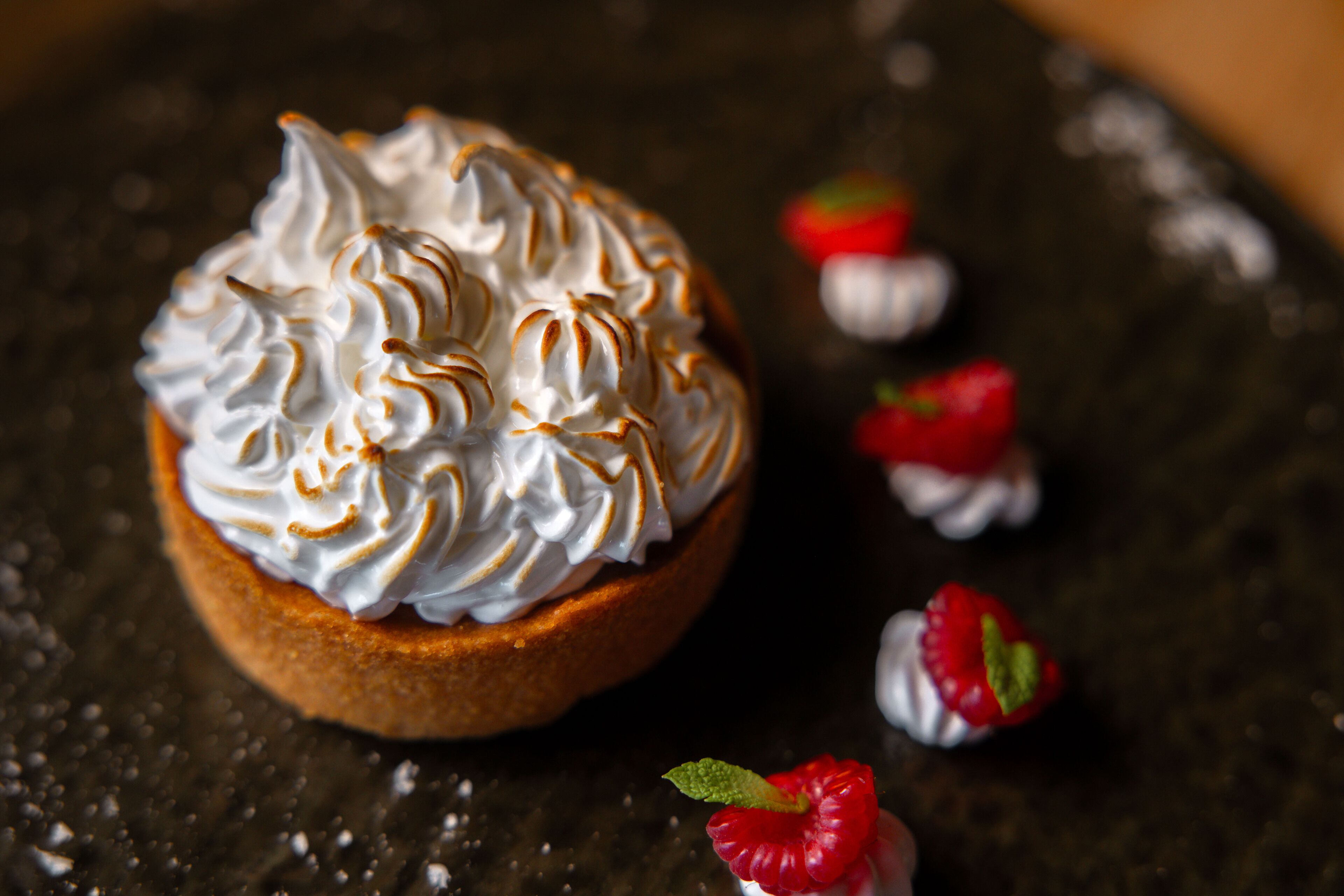 Postre con crema batida y una fresa como decoración en un plato oscuro.