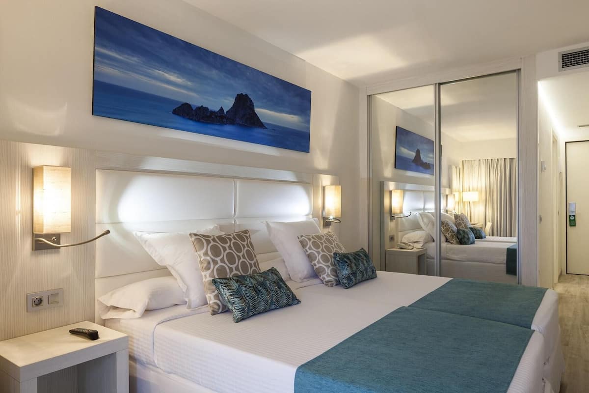 A hotel room with a large bed, two bedside tables, a nightstand, a wall-mounted TV, and a large window.