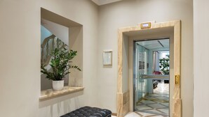 A hallway with a marble floor, a black leather bench, a potted plant, and a door leading to another room. - My City Hotel (Tallinn)