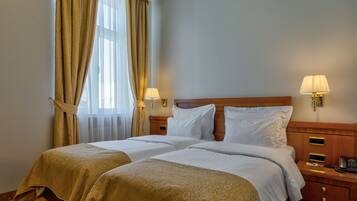 A hotel room with two beds, a wooden headboard, bedside lamps, a nightstand with a phone, and a window with curtains.