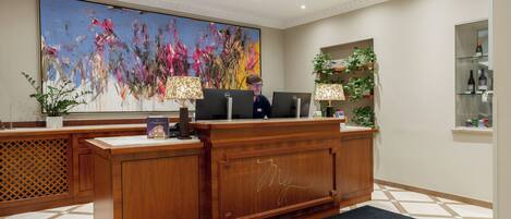 A reception desk with a large abstract painting, a wooden counter, and a carpet with 'My Hotel' text.