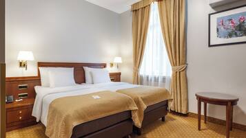 Habitación de hotel con cama doble, mesitas de noche, una mesita pequeña y una ventana con cortinas.