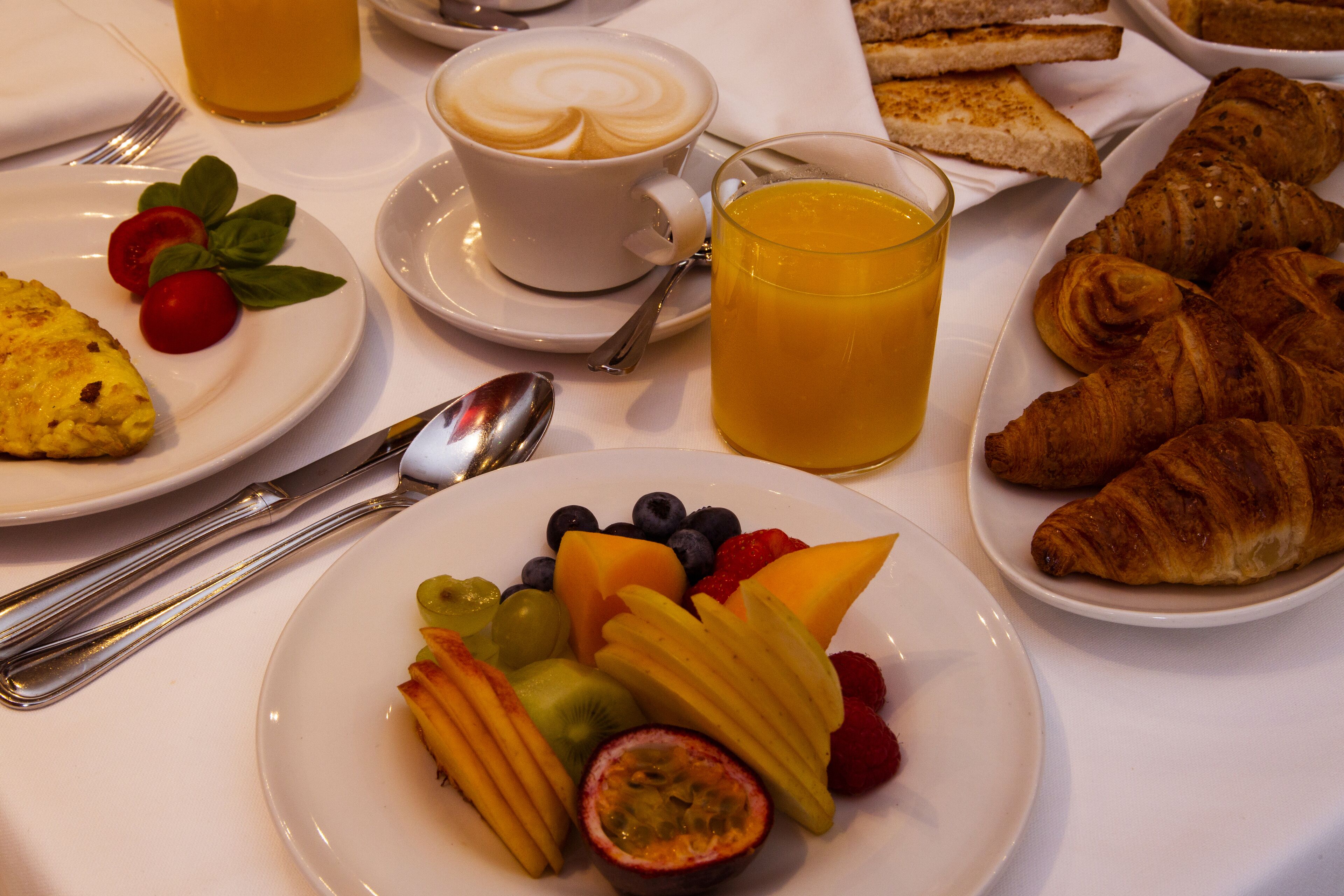 Uma mesa de café da manhã com pratos de frutas, croissants e uma xícara de café.