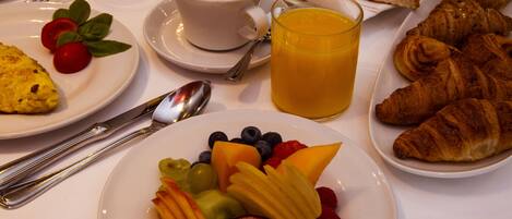 Uma mesa de café da manhã com pratos de frutas, croissants e uma xícara de café.