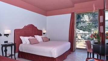 A hotel room with a large bed, a desk, a chair, and a view of a mountainous landscape.