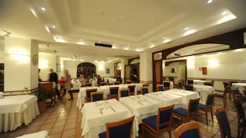 Un comedor amplio con varias mesas y sillas, piso de baldosas y un techo alto con iluminación empotrada.
