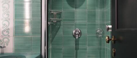 A modern bathroom with a glass-enclosed shower, a white bathtub, and a green-tiled wall.
