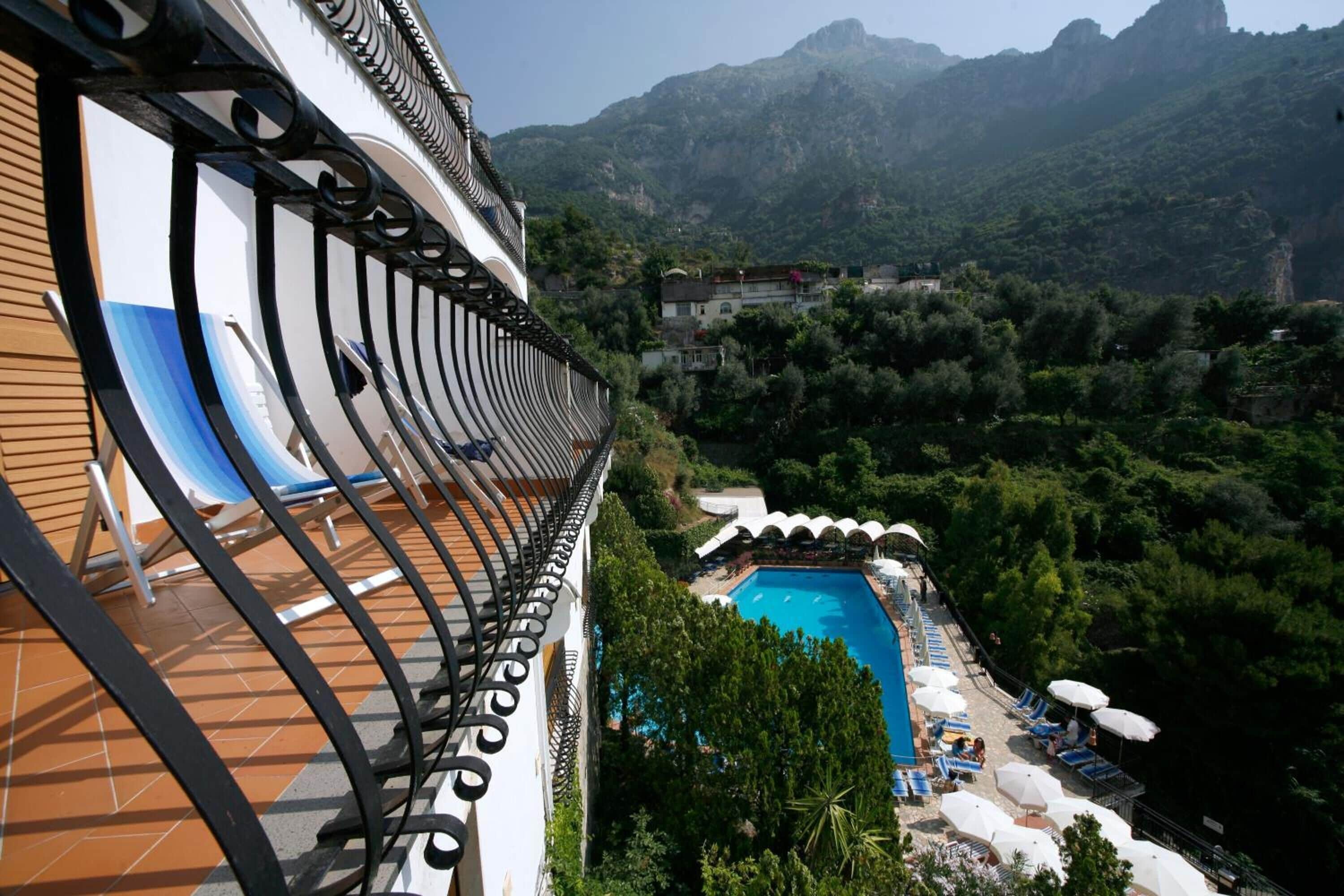 A hotel balcony with a pool and lounge chairs.