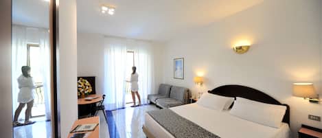 A hotel room with a bed, a sofa, a desk with a chair, and a window with curtains.