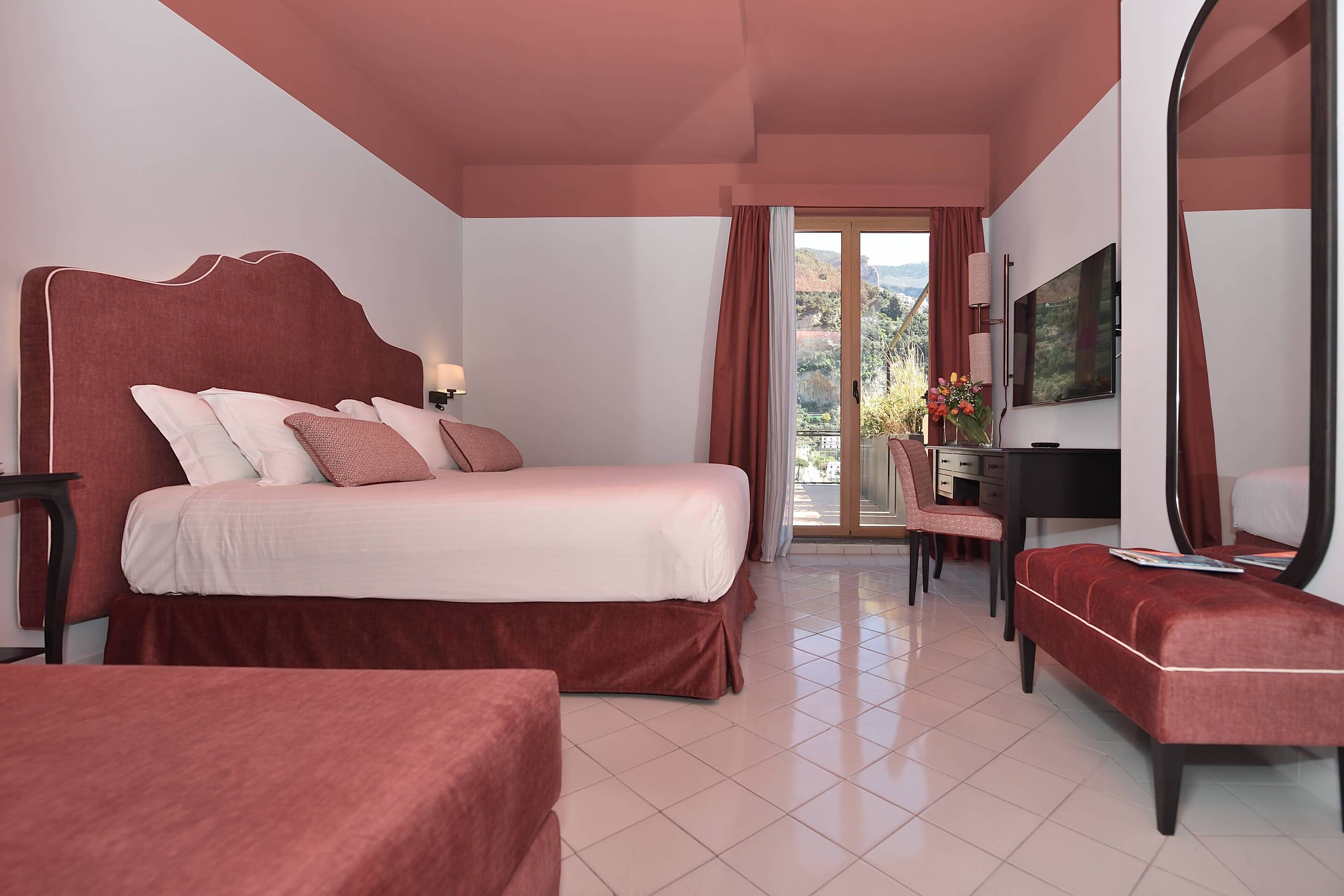 Een hotelkamer met een groot bed, een bureau met een stoel, een televisie en een balkon met uitzicht.