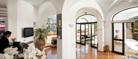 A hotel lobby with arched ceilings, a reception desk, a TV, and a large window offering a view of the outdoors.