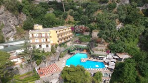 An aerial view of a resort with a central swimming pool, multiple buildings with balconies, and lush greenery surrounding the area. - Hotel Royal Positano (Positano)