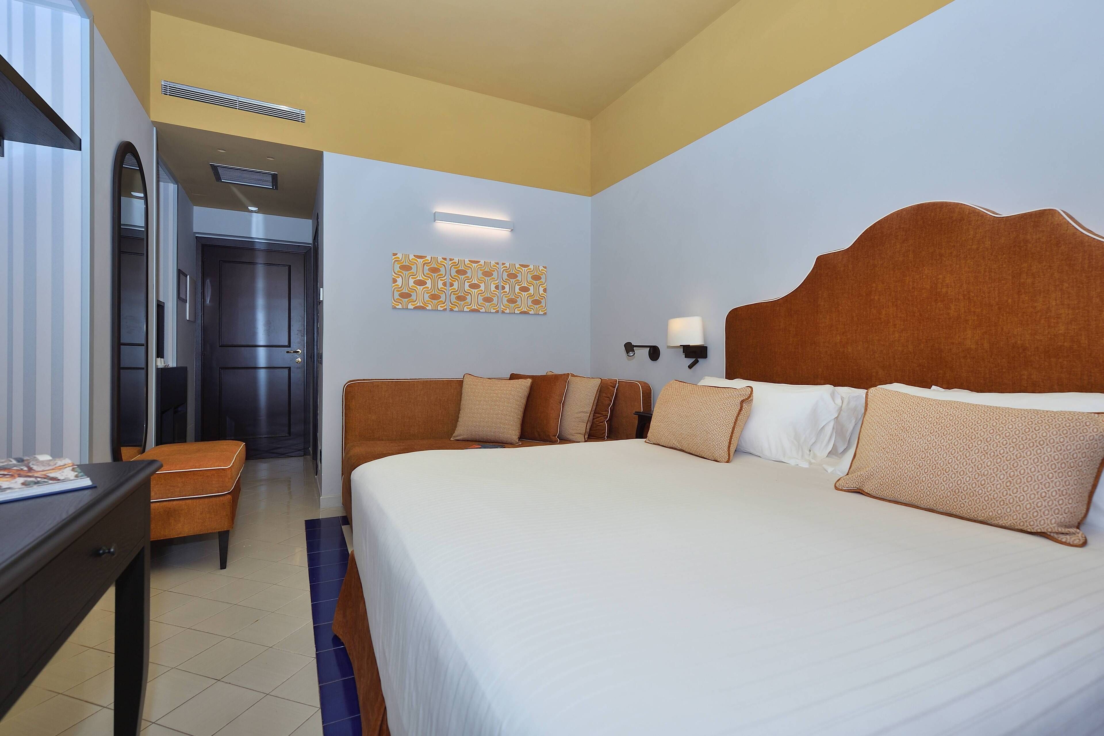Habitación de hotel con una cama grande, un escritorio, una silla y una puerta que da a otra habitación.