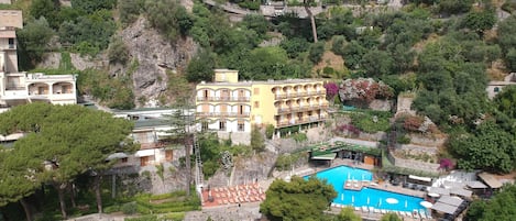 A hillside hotel with a swimming pool, terraced gardens, and a view of the surrounding town.