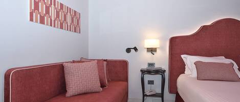 A room with a red sofa, a bed with a headboard, a bedside table with a lamp, and a wall art piece.