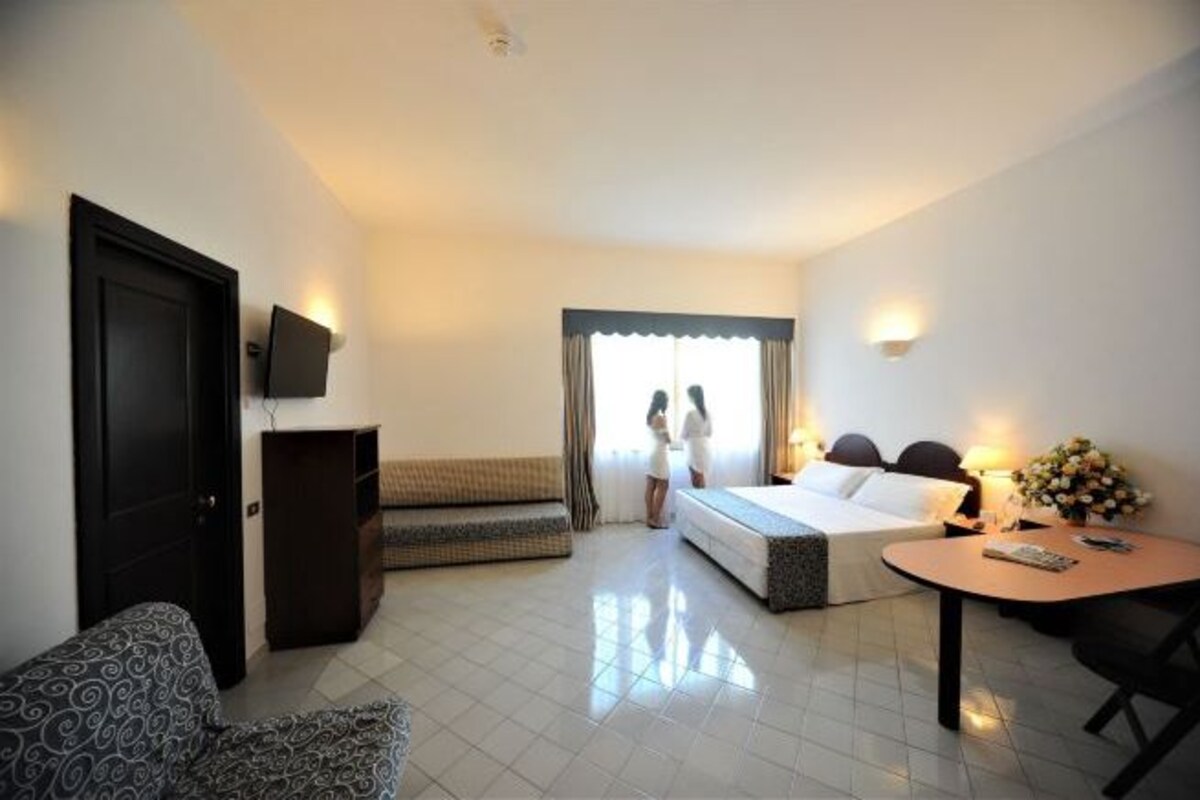 A hotel room with a bed, a sofa, a small table, a TV, and a window with curtains.