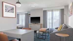 A modern hotel room with a dining area, a sofa, a TV, and a desk. - Homewood Suites by Hilton Detroit-Troy (Troy)