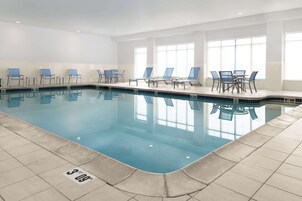 Una piscina interior con agua cristalina, suelo de baldosas y sillas azules a lo largo de la piscina.