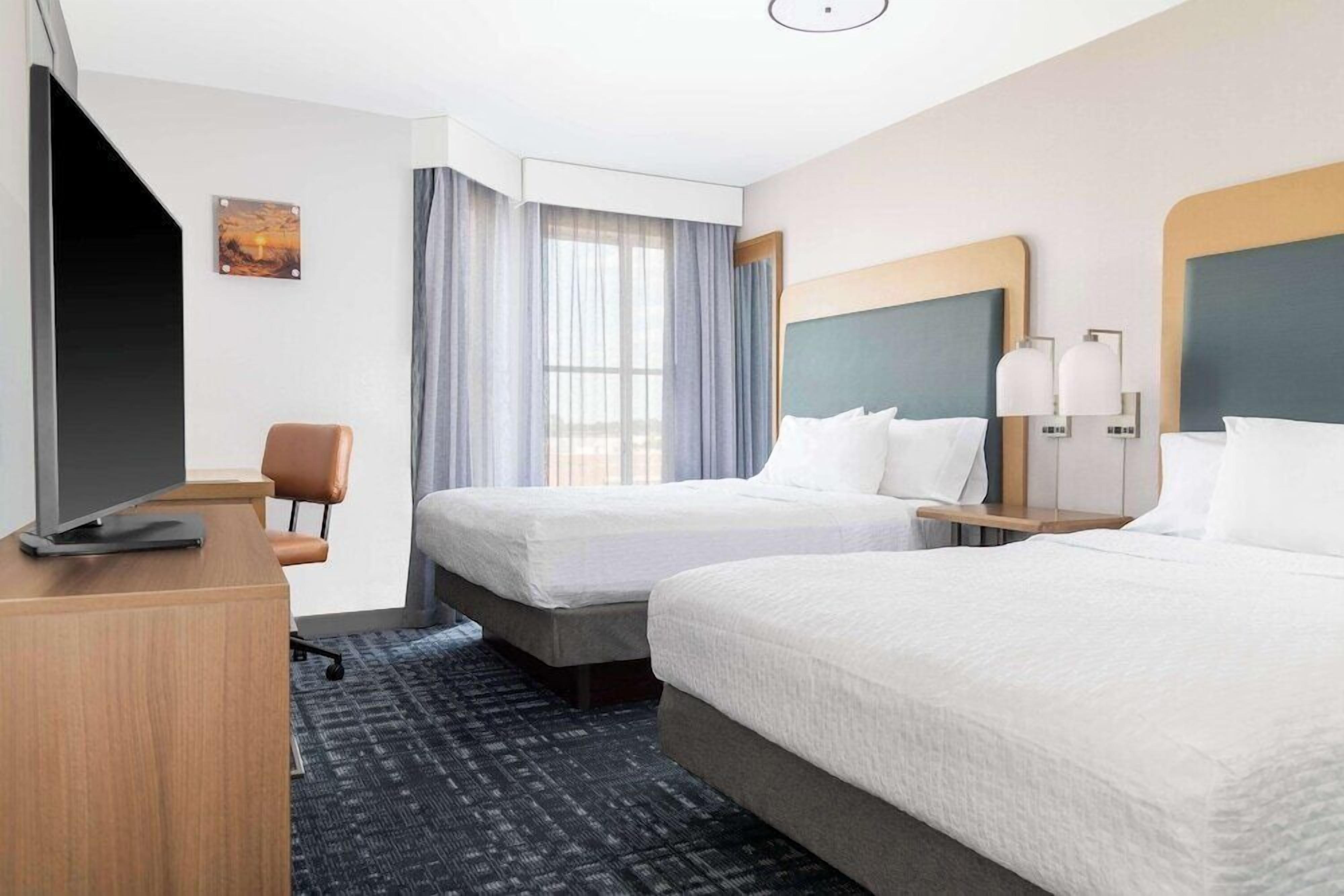 A hotel room with two beds, a desk, a chair, a TV, and a window with curtains.
